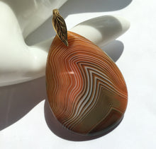 Load image into Gallery viewer, Orange and Brown Onyx pendant in a pear shape with gold plated leaf bail.